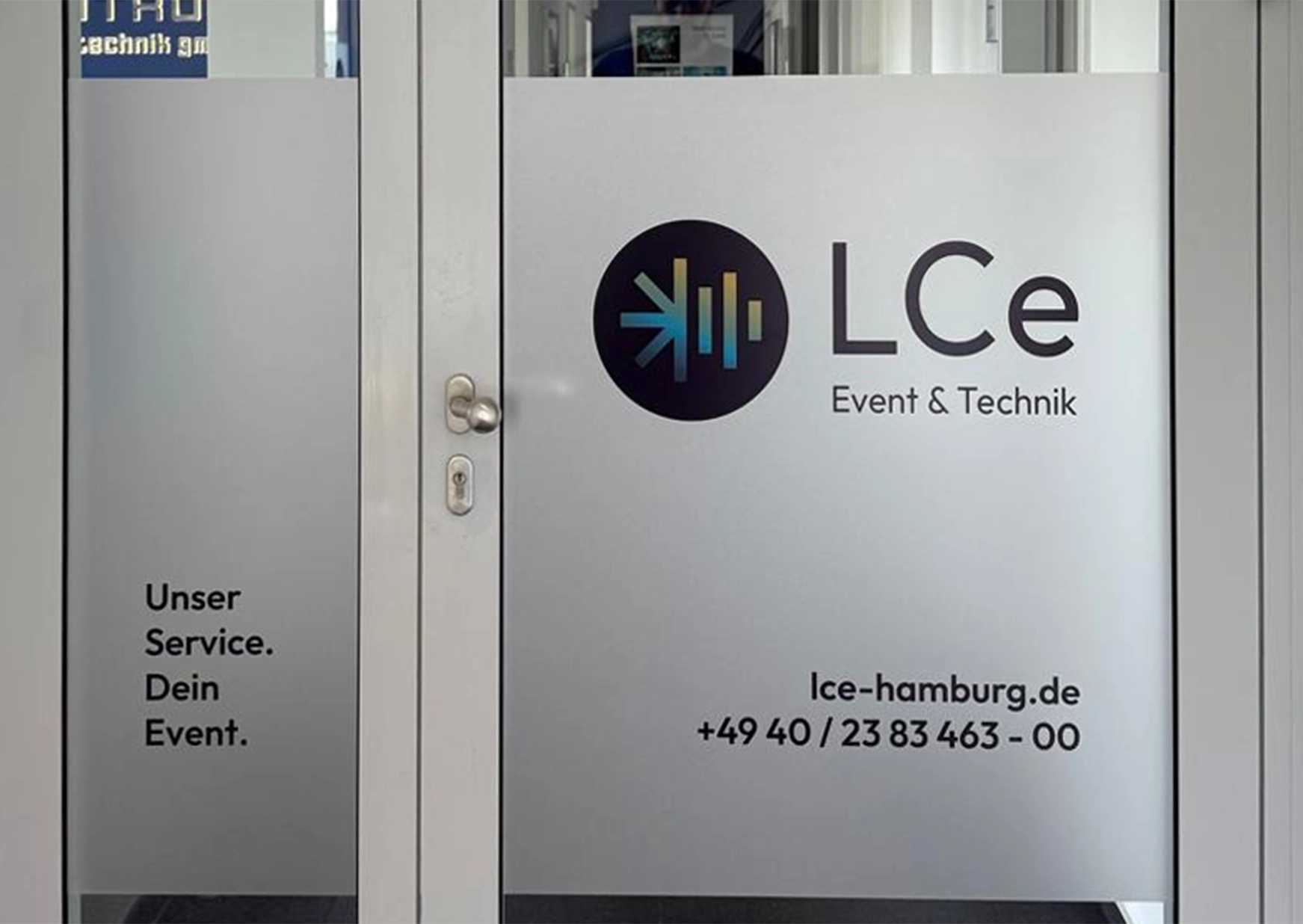 Eine gläserne Tür ist mit Milchglasfolie beklebt, auf der das Logo zu sehen ist.